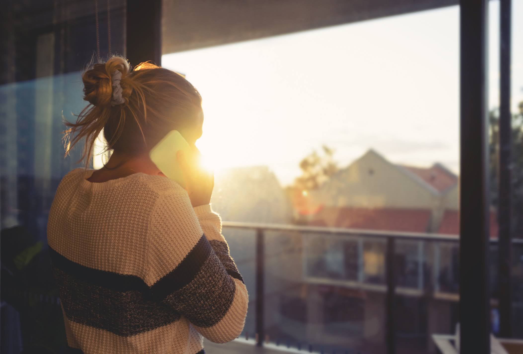 Young woman talking on the phone looking out a window.